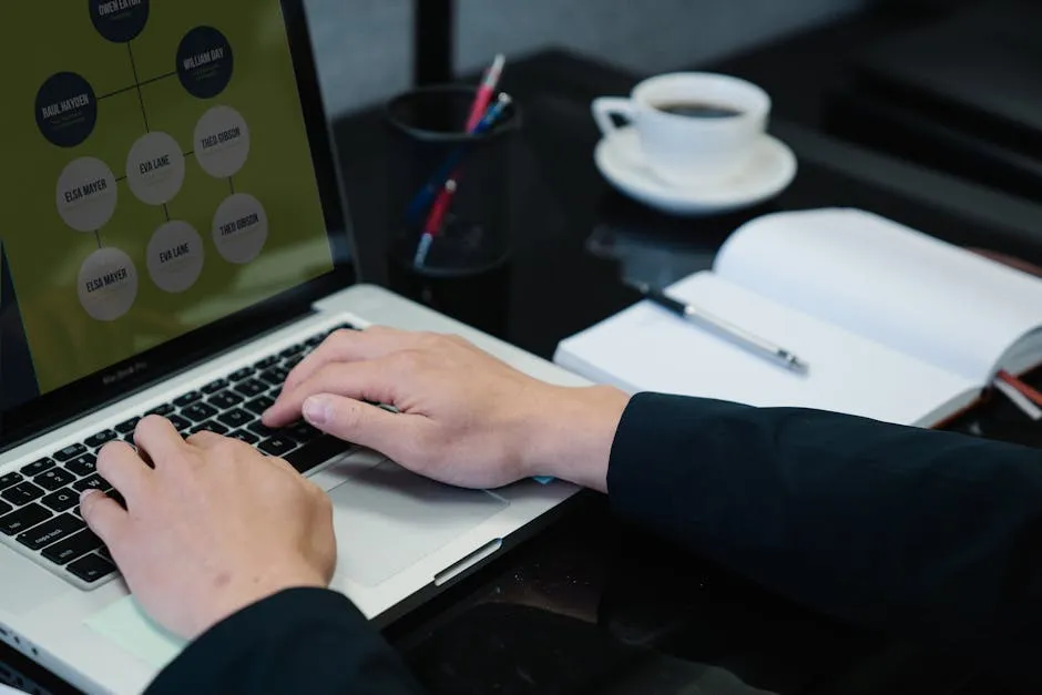 Close-up of hands typing on a laptop displaying an organizational chart, a notebook, and coffee nearby. — Photo by Felicity Tai on Pexels