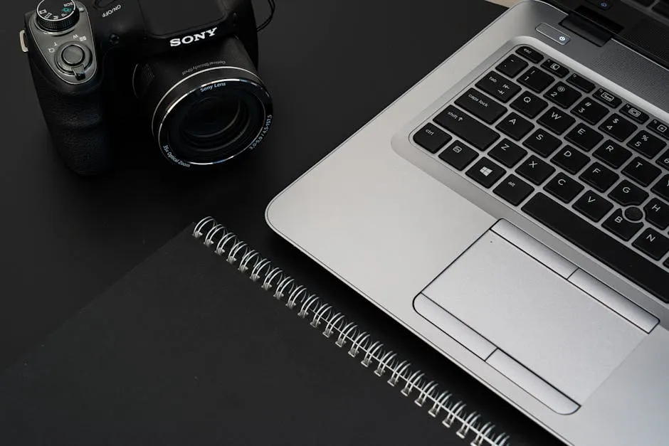 A stylish office desk featuring a laptop, camera, and spiral notebook on a dark surface. — Photo by Castorly Stock on Pexels
